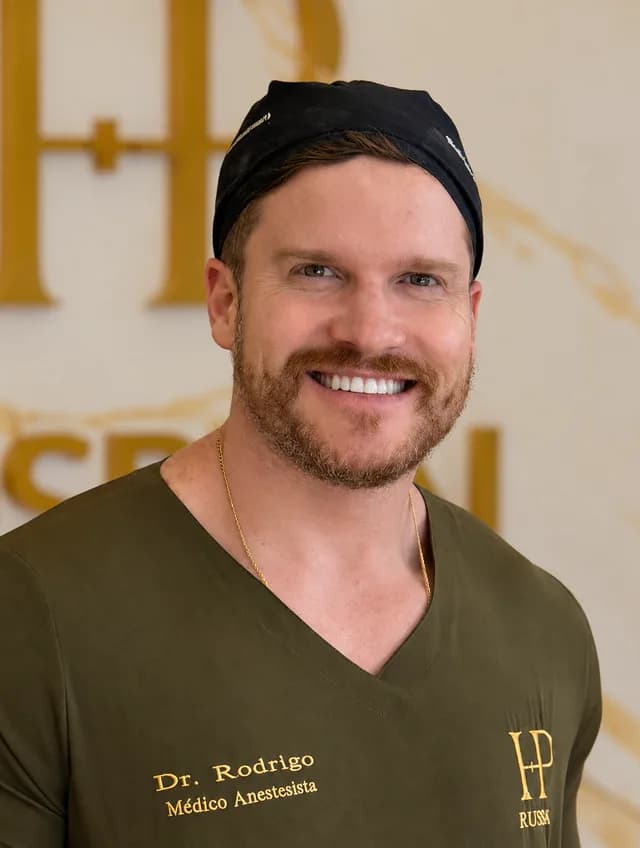 Dr. Rodrigo Delfino, de uniforme verde-oliva e touca cirúrgica preta, sorrindo