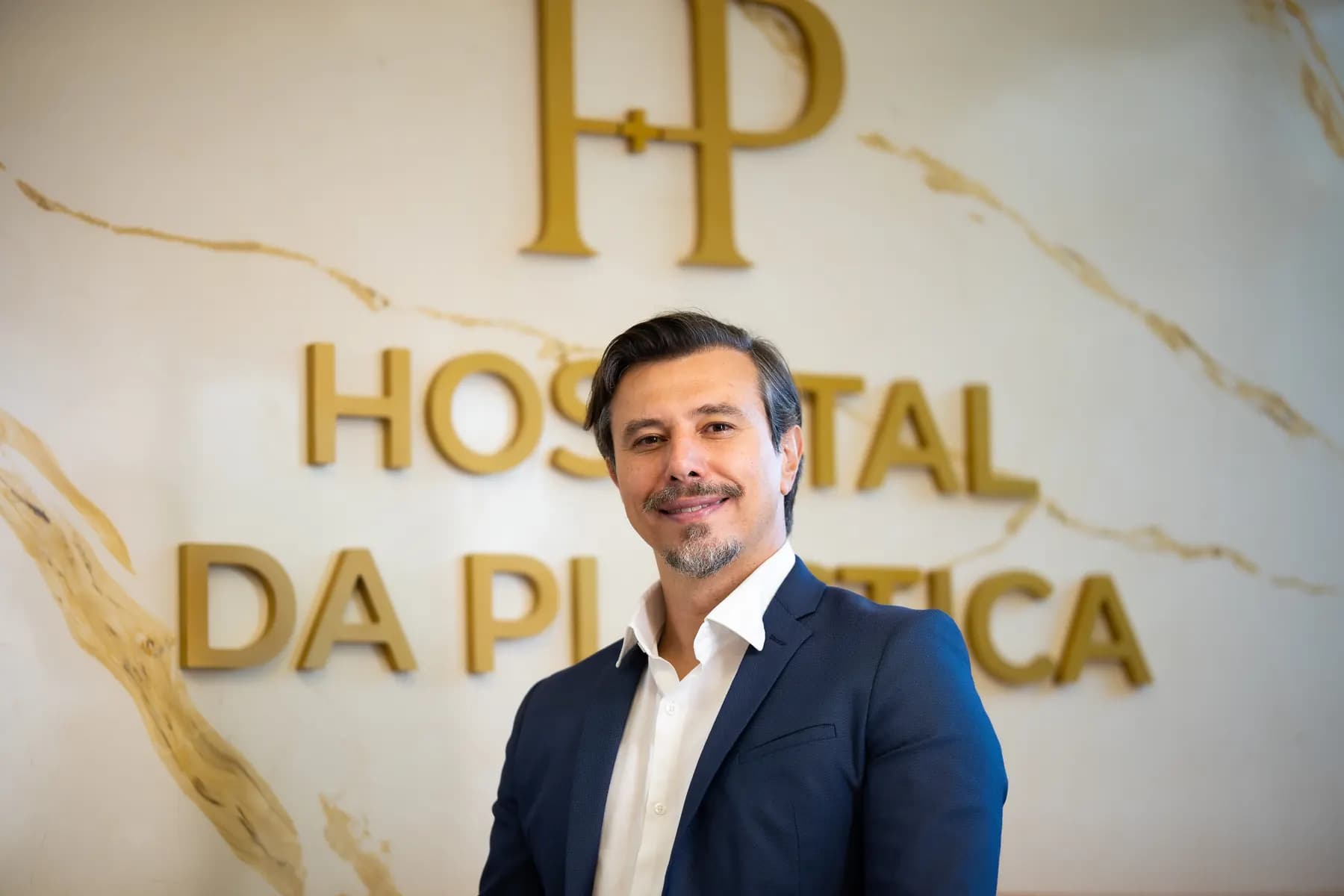 Dr. Mário Russano diante da parede com o logotipo do hospital